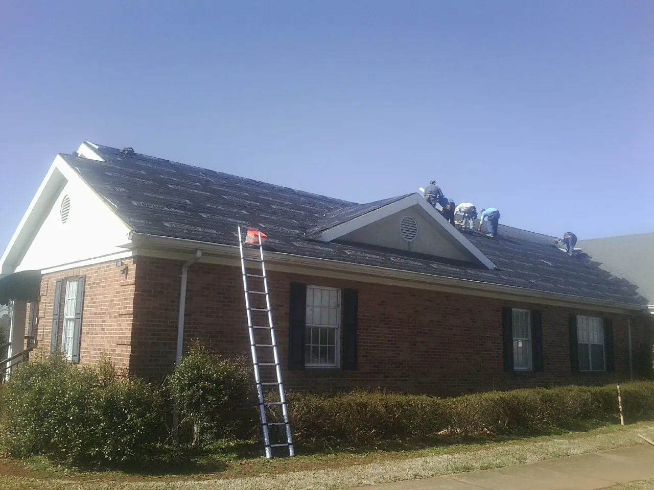 Crew tearing shingles off a brick ranch roof with a ladder set — Metal Roof Repair work by our crew in South Jordan