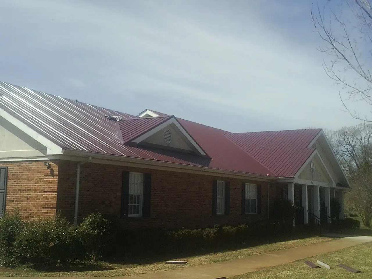 Red metal roof with gabled entries on a long brick building, from a Hail Damage Roof Repair job in South Jordan