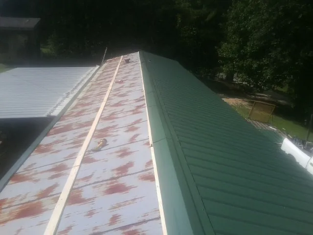 Old rusted panels beside newly installed green metal roofing in South Jordan