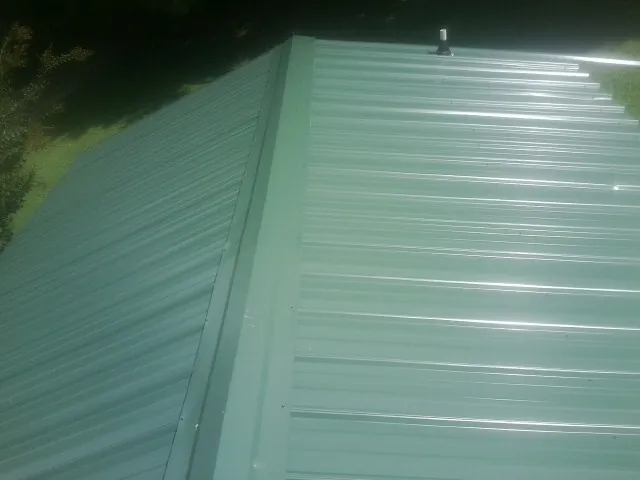 New green metal panels meeting at the ridge of a roof — Flat Roof Repair work by our crew in South Jordan