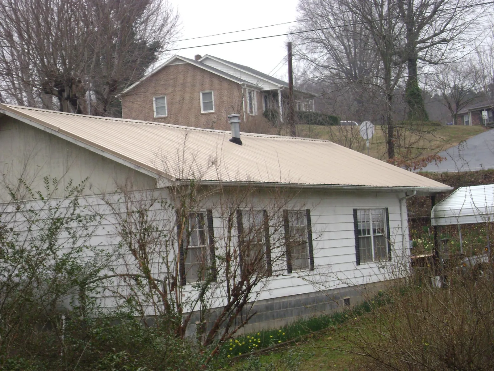Tan metal roof on a white sided house set into a hillside — Commercial Roofing by Roofing Brothers in South Jordan